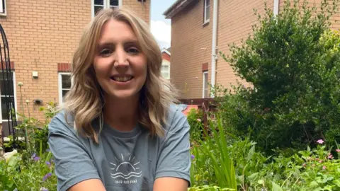 Rachel Griffiths Rachel is sat in her garden, smiling. She has blonde hair and is wearing a grey/blue t-shirt.